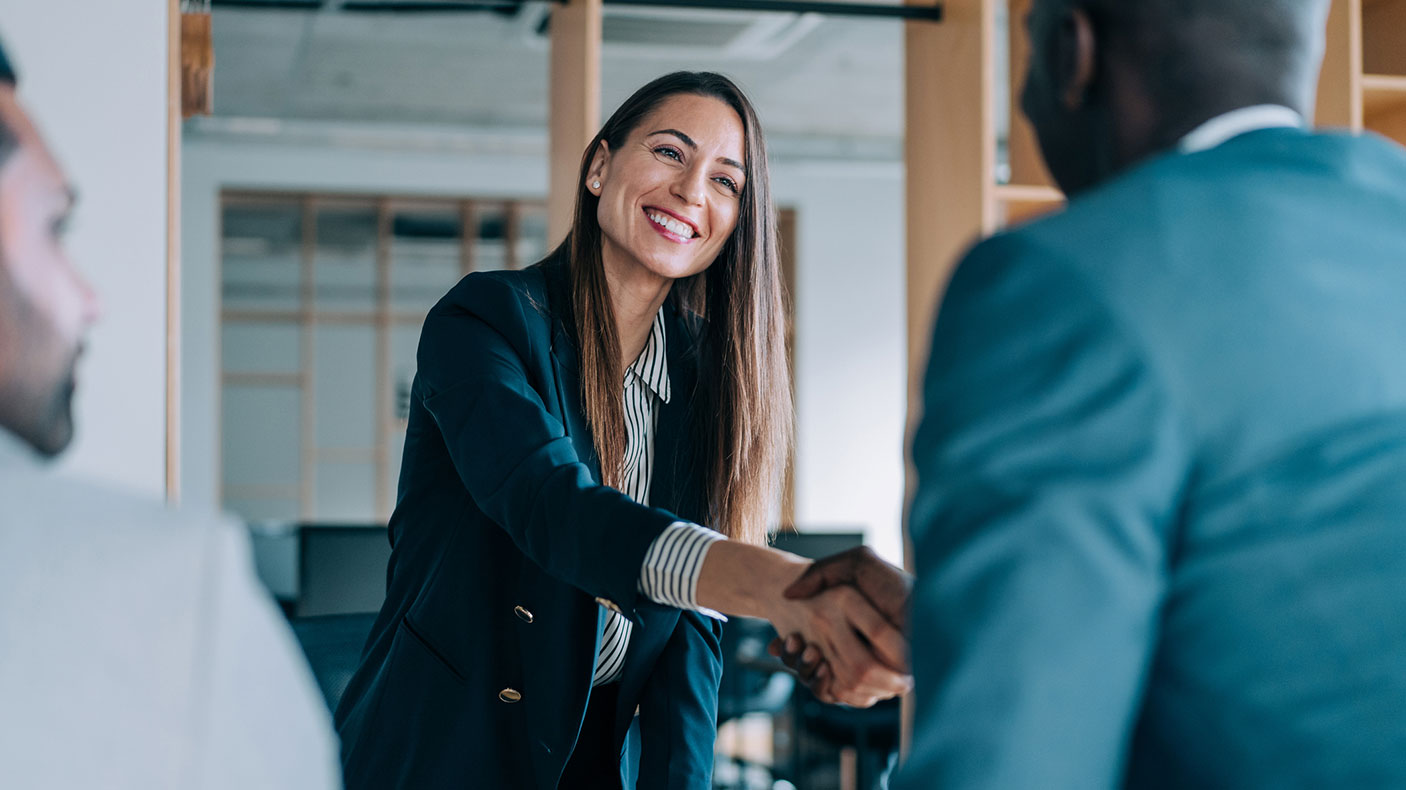 Woman leans over desk and shakes the hand of a man visiting her office