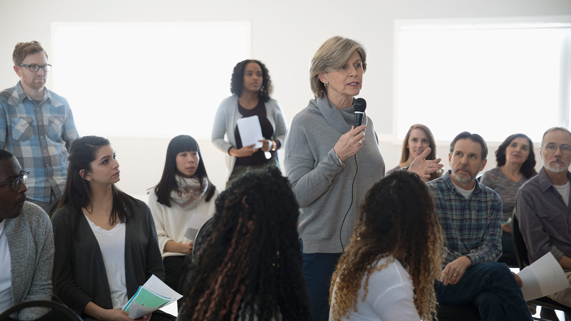 A woman standing up in an audience speaking into a microphone